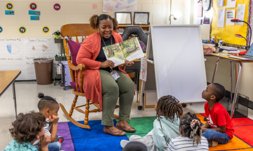 Keecha Finley sits in a rocking chair and reads a book with her students in front of the classroom.